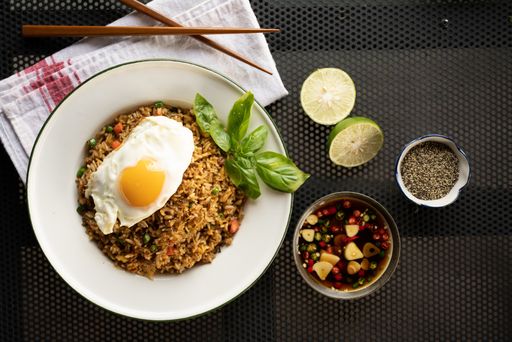 An overhead shot of a dish with rice, egg and vegetable leaf on a white round plate near the salad