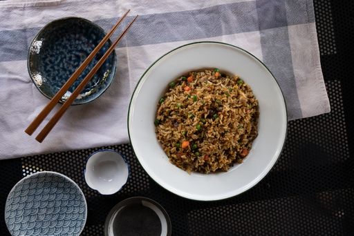 An overhead shot of a dish with rice and vegetables near chopsticks