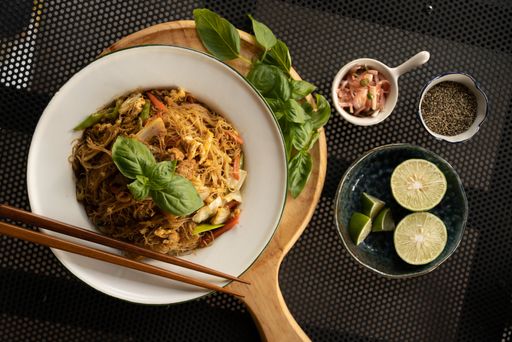 An overhead shot of a dish with noodles and vegetables near spices and lemons