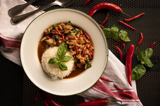 An overhead shot of a dish with rice and sliced onions in the white plate near red peppers