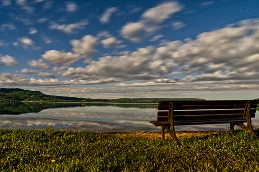 A beautiful shot of a seascape and a bench under the cloudy skies
