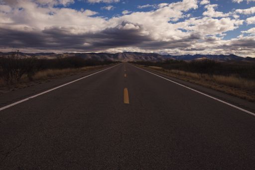A landscape of a highway surrounded by hills and fields under the sunlight in Arizona, the US