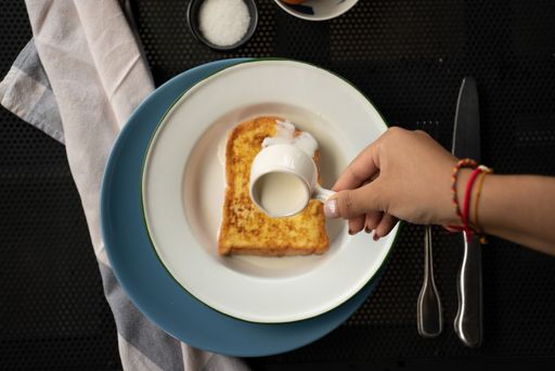 An overhead shot of a person pouring cream on top of a french toast on a round white plate