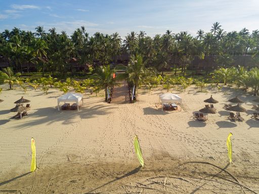 A high angle shot of lounge chairs on a sandy surface with shade tents nad umbrellas on a sunny day