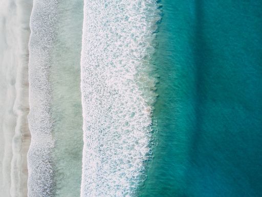 An aerial shot of sea waves hitting the shore at daytime