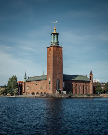 A view of blue water and the Stockholm City Hall on the other side with a blue horizon sky