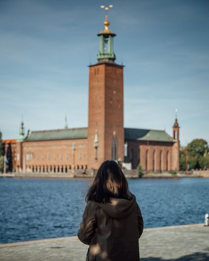 A view of a woman looking at the Stockholm City Hall on the other side with a blue horizon sky