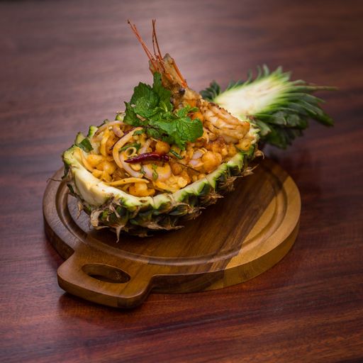 A vertical shot of a dish with shrimp and vegetable leaf in a pineapple on a wooden plate