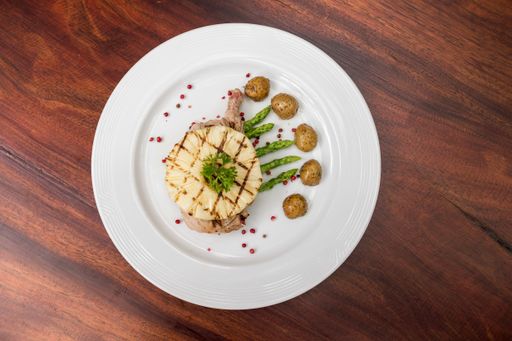 An overhead shot of grilled pineapple slice on the meat on a white plate