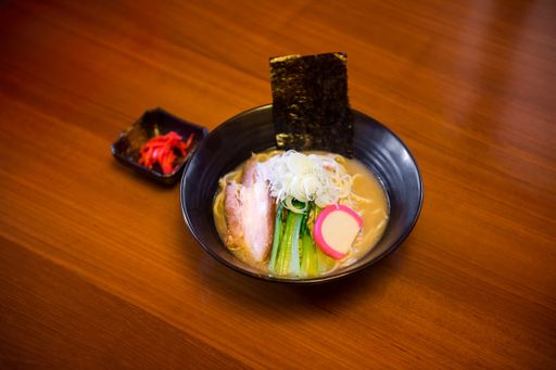 A high anlger shot of a soup with noodles, meat, and vegetables in a black bowl with a blurred background