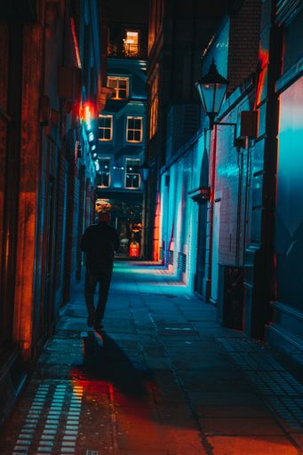 A vertical shot of a man walking on a neon-lit alley.