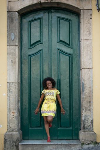 A vertical shot of an African female model with curly hair dancing in front of a green door in Brazil