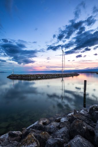 A vertical shot of a rocky shore in the middle of the water under a blue sky