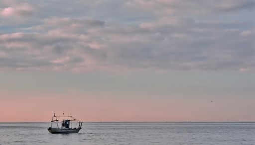 A small fishing boat in the sea against a cloudy sky during the sunset