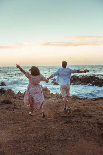 A vertical back view of a beautiful couple running guided by their love at the beach in Corsica, France