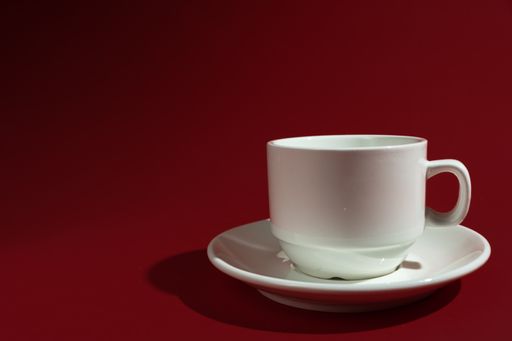 A closeup shot of a white cup and saucer isolated on red background