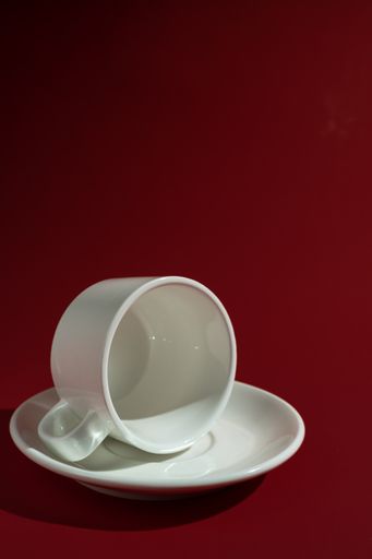 A vertical shot of a white cup and saucer isolated on red background