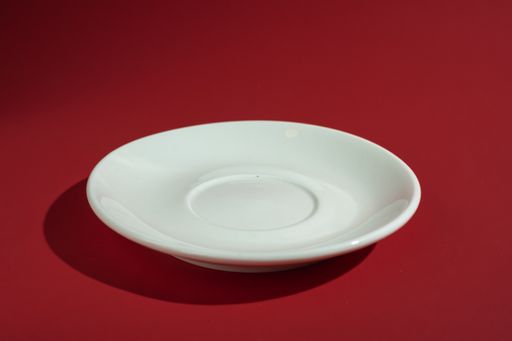 A closeup of a white saucer on a red surface