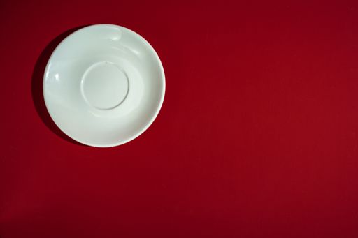 A top view of a white saucer on a red surface
