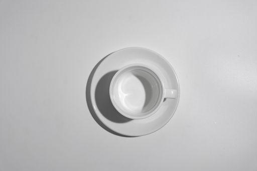 A top view of a white empty cup and saucer on a white surface