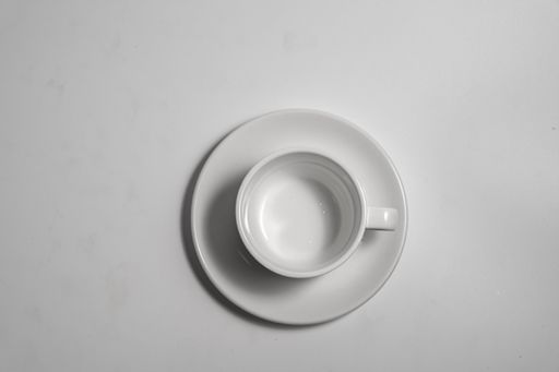 A top view of a white empty cup and saucer on a white surface