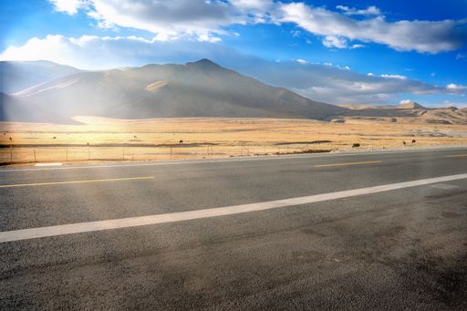 A scenic shot of an empty road in the middle of a dry plain field