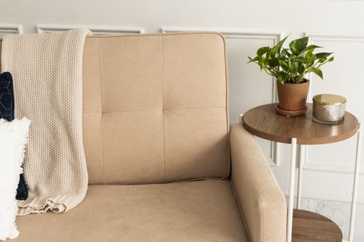 A small round table with a potted plant and a candle near a brown sofa