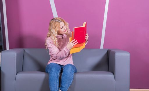 A young Caucasian surprised female sitting on a sofa and reading a book