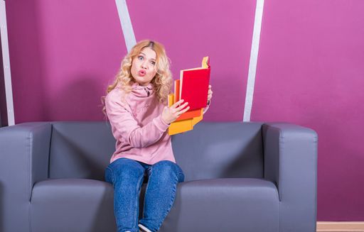 A young Caucasian surprised female sitting on a sofa and reading a book