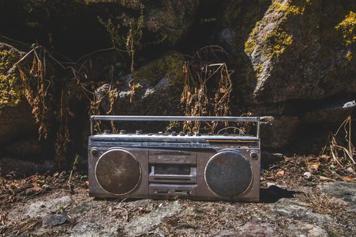 A retro outdated portable stereo boombox radio cassette recorder on the ground around mossy stones