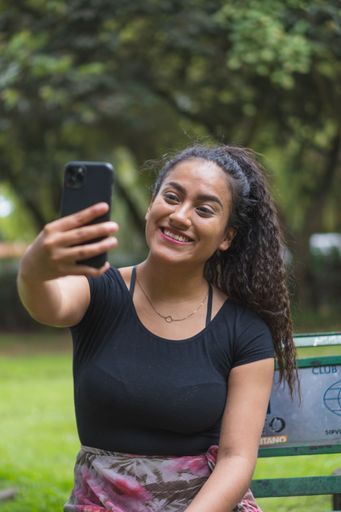 A vertical shot of a Hispanic young female taking a selfie in a park