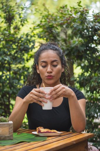 A vertical shot of a Hispanic young female enjoying tea in a park
