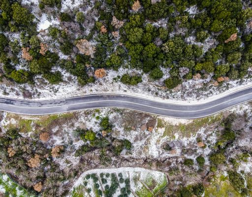 An aerial shot of the traffic road passing through the dense forest on a cold snowy day