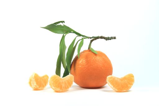 A closeup of a tangerine with leaf and some wedges on a white background