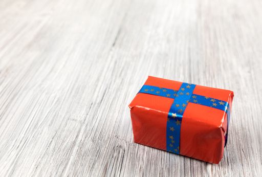 A closeup shot of a red gift with blue ribbon on a wooden surface
