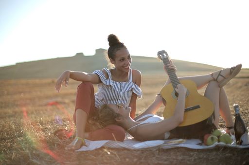 Two young female friends having fun in the picnic and playing the guitar