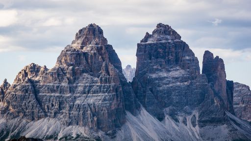 A beautiful shot of the Tre cime di lavaredo mountains with a cloudy sky in the background