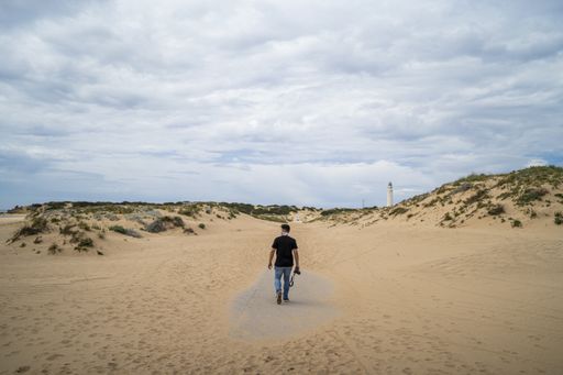 A male photographer walking through a beach under a cloudy sky at daytime in Andalusia, Spain
