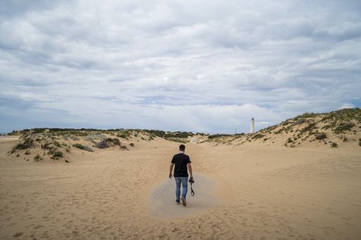 A male photographer walking through a beach under a cloudy sky at daytime in Andalusia, Spain