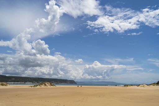 The beach surrounded by the sea and hills covered in greenery under a blue cloudy sky in Andalusia, Spain