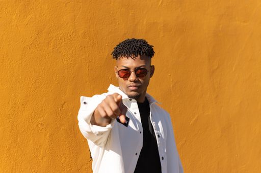 A young handsome hispanic black male posing near a yellow wall pointing at the camera