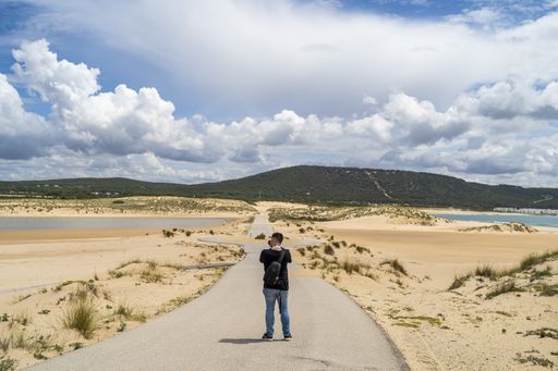 A male photographer walking through a beach under a cloudy sky at daytime in Andalusia, Spain