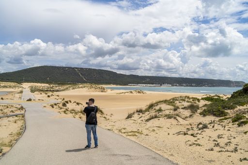 A male photographer walking through a beach under a cloudy sky at daytime in Andalusia, Spain