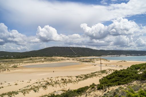 A landscape of a beach surrounded by the sea and hills covered in greenery under a blue cloudy sky at daytime
