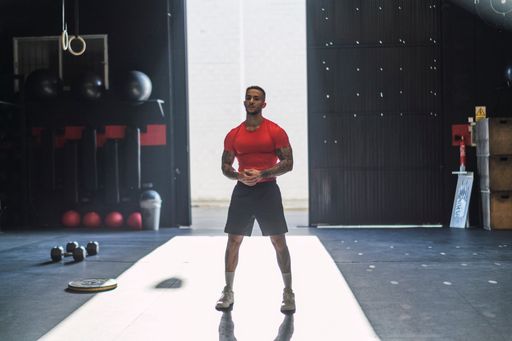 A vertical shot of an athlete posing in the gym in a red workout shirt