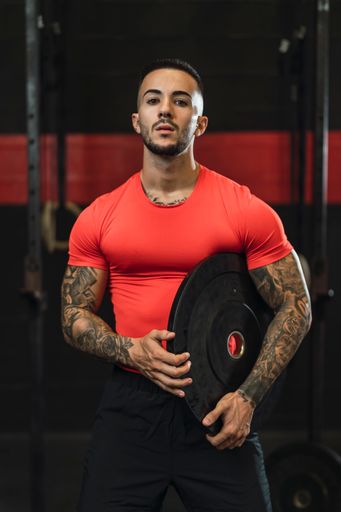 Vertical shot of an athlete posing in the gym in a red workout shirt
