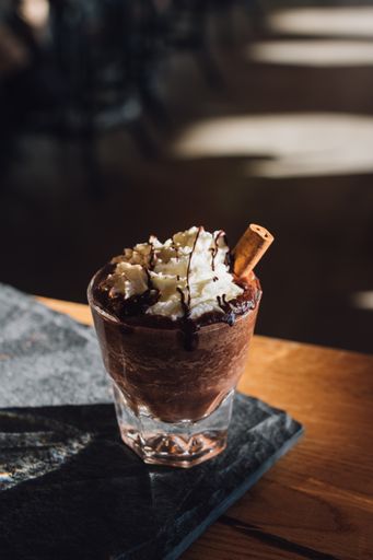 A hot chocolate topped with whipped cream, chocolate drizzle, cinnamon stick on wood table