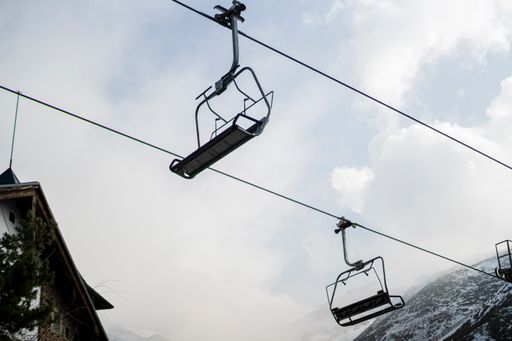 A bottom shot of an empty ropeway seat in the background of a cloudy sky.