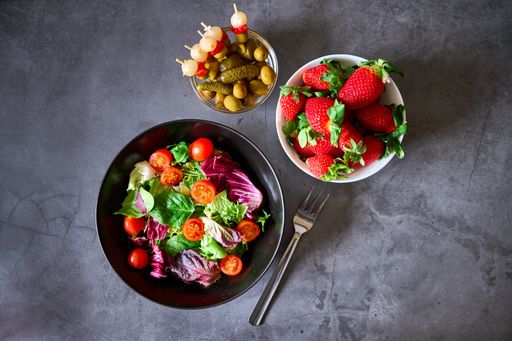 A top view of a vegetable salad, chips, pickles and strawberries on a marble table