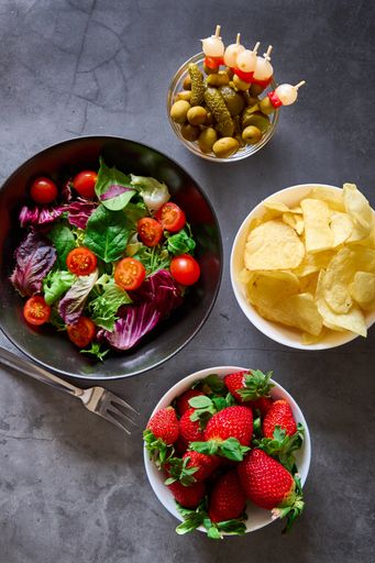 A top view of a vegetable salad, chips, pickles and strawberries on a marble table